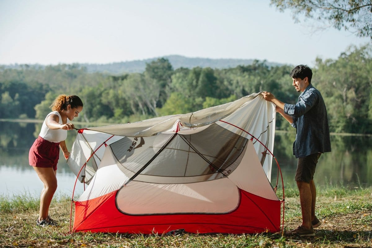 Two people setting up a two-person tent at a flat campsite